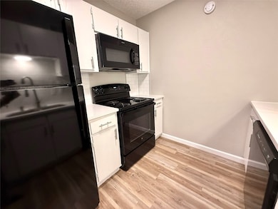 Kitchen featuring black appliances, light countertops, light wood finished floors, white cabinetry, and decorative backsplash