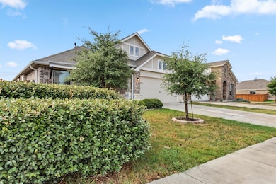 View of property hidden behind natural elements featuring driveway, a garage, and brick siding