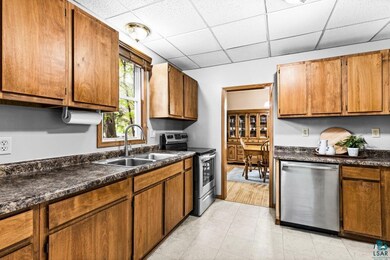 Kitchen with stainless steel appliances, a sink, dark countertops, a drop ceiling, and brown cabinetry