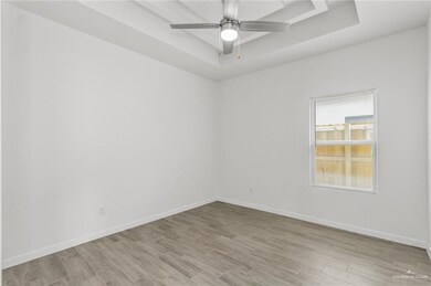 Empty room with a ceiling fan, baseboards, a raised ceiling, and light wood-type flooring