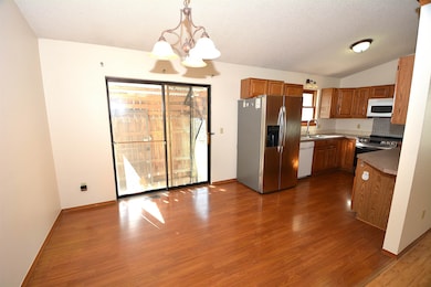 Kitchen with brown cabinetry, hanging light fixtures, appliances with stainless steel finishes, a chandelier, and dark wood-style floors