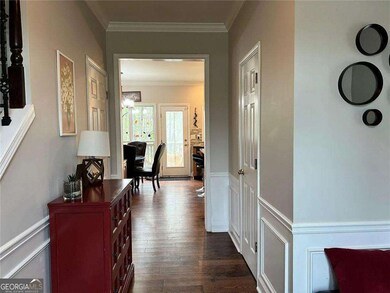 Hallway featuring crown molding, dark wood-type flooring, wainscoting, and a decorative wall