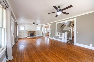 Unfurnished living room with built in features, a stone fireplace, ceiling fan, and dark hardwood / wood-style flooring