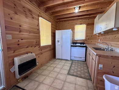 Kitchen with sink, beamed ceiling, heating unit, wood walls, and white appliances