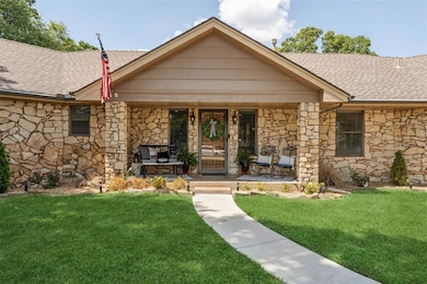 View of front of home featuring roof with shingles, stone siding, covered porch, and a front lawn
