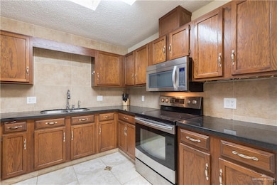 Kitchen with appliances with stainless steel finishes, brown cabinets, backsplash, a textured ceiling, and light tile patterned floors
