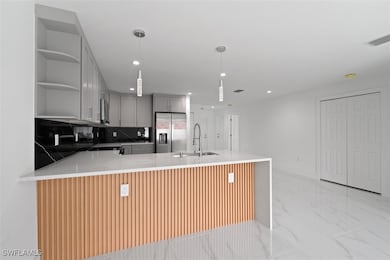 Kitchen featuring gray cabinetry, light stone counters, a peninsula, tasteful backsplash, and hanging light fixtures