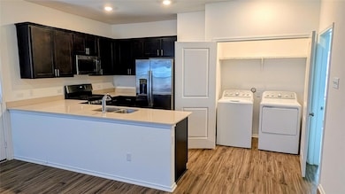 Kitchen with stainless steel appliances, light stone counters, light wood finished floors, washer and clothes dryer, and a peninsula