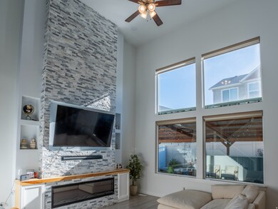 Living area with a fireplace, a ceiling fan, wood finished floors, and a high ceiling