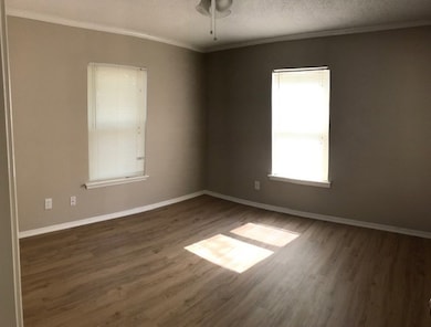 Empty room featuring a textured ceiling, ornamental molding, wood finished floors, and a ceiling fan
