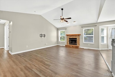 Unfurnished living room featuring a fireplace, vaulted ceiling, wood finished floors, and a ceiling fan