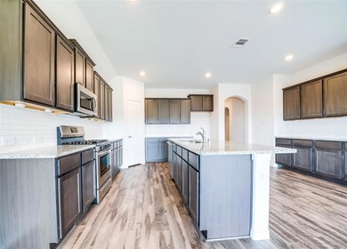 Kitchen featuring dark brown cabinets, light wood-type flooring, a center island with sink, and appliances with stainless steel finishes