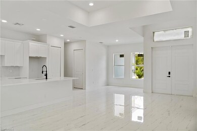 Kitchen featuring light marble finish flooring, tasteful backsplash, white cabinetry, light countertops, and an island with sink