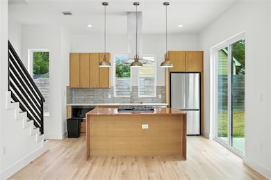 Kitchen featuring light stone counters, a center island, freestanding refrigerator, pendant lighting, and decorative backsplash