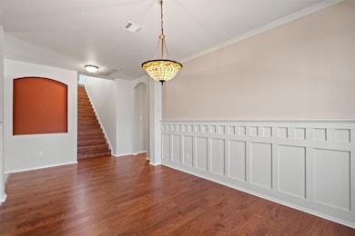 Unfurnished dining area featuring arched walkways, ornamental molding, dark wood-style flooring, stairs, and a decorative wall
