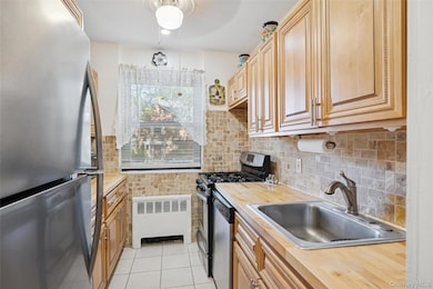 Kitchen featuring appliances with stainless steel finishes, light countertops, radiator, light tile patterned floors, and backsplash