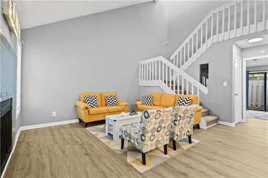 Living room featuring light wood-style floors, stairs, baseboards, a fireplace, and a towering ceiling