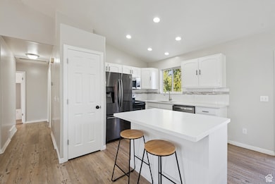 Kitchen featuring lofted ceiling, appliances with stainless steel finishes, white cabinetry, tasteful backsplash, and a breakfast bar