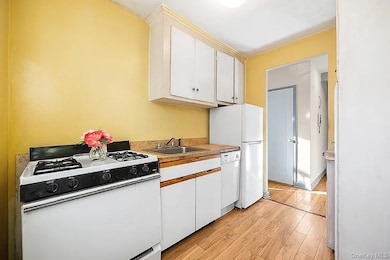 Kitchen with white appliances, white cabinetry, light wood-style flooring, and light countertops