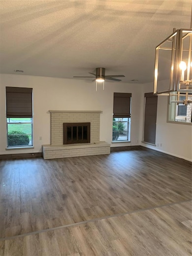 Unfurnished living room with a textured ceiling, a brick fireplace, wood finished floors, and a ceiling fan