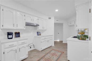 Kitchen featuring tasteful backsplash, white cabinetry, light countertops, recessed lighting, and light wood finished floors