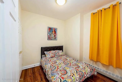Bedroom with wood finished floors and a baseboard heating unit