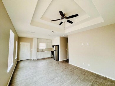 Unfurnished living room with a tray ceiling, a ceiling fan, light wood finished floors, and plenty of natural light