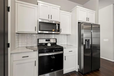 Kitchen with white cabinetry, appliances with stai