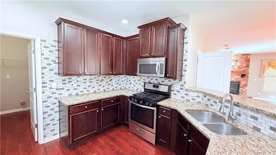 Kitchen featuring decorative backsplash, stainless steel appliances, light stone countertops, dark wood-style flooring, and a stone fireplace