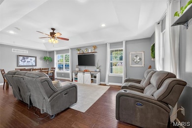 Living area featuring a raised ceiling, dark wood finished floors, recessed lighting, and a ceiling fan
