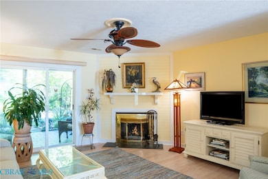Living room featuring light wood finished floors, a textured ceiling, a ceiling fan, and a large fireplace