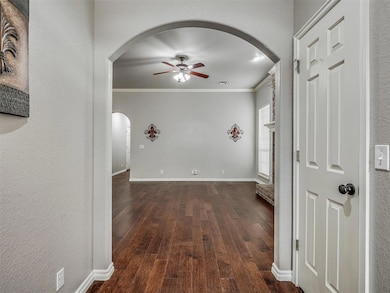 Corridor with arched walkways, ornamental molding, dark wood finished floors, baseboards, and a textured wall