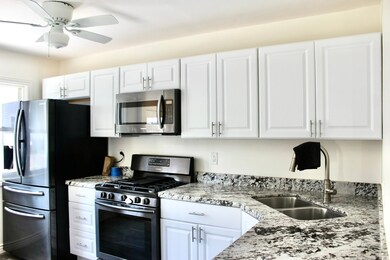 Kitchen with stainless steel appliances, white cabinets, and light stone counters