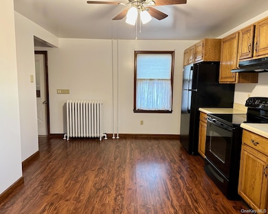 Kitchen featuring black / electric stove, brown cabinetry, light countertops, and radiator