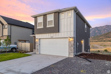 View of front facade featuring stone siding, concrete driveway, an attached garage, board and batten siding, and stucco siding