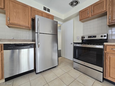 Kitchen featuring backsplash, brown cabinetry, stainless steel appliances, and light countertops