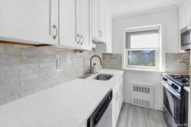 Kitchen featuring appliances with stainless steel finishes, backsplash, white cabinets, and radiator