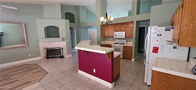 Kitchen featuring brown cabinets, white appliances, a kitchen breakfast bar, high vaulted ceiling, and tile counters