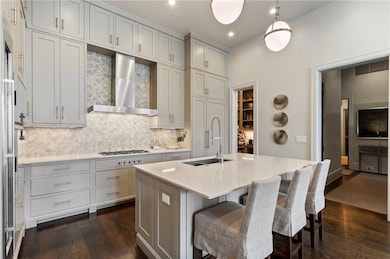 Kitchen featuring dark wood-style floors, backsplash, wall chimney range hood, a breakfast bar, and recessed lighting