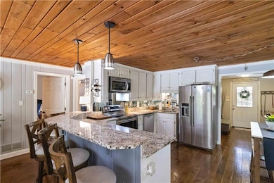 Kitchen with appliances with stainless steel finishes, a peninsula, white cabinets, wooden ceiling, and light stone counters