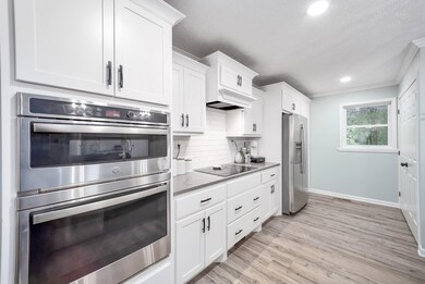 Kitchen with appliances with stainless steel finishes, white cabinets, light wood finished floors, backsplash, and a textured ceiling