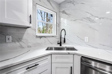 Kitchen featuring stainless steel dishwasher, backsplash, white cabinetry, and light stone countertops
