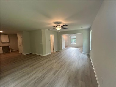 Unfurnished living room featuring baseboards, ceiling fan, and light wood-style flooring