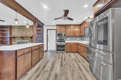 Kitchen featuring appliances with stainless steel finishes, brown cabinetry, ceiling fan, decorative light fixtures, and light wood finished floors
