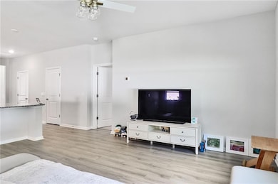 Living room featuring light wood-type flooring, a ceiling fan, baseboards, and recessed lighting