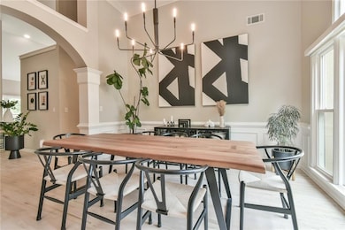 Dining space featuring arched walkways, a towering ceiling, light wood finished floors, ornate columns, and wainscoting
