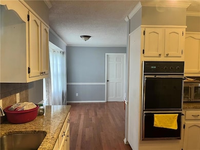 Kitchen with dark wood-type flooring, light stone countertops, ornamental molding, wainscoting, and white cabinets