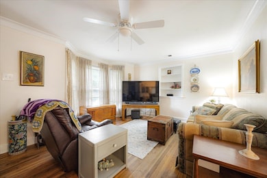 Living area with light wood finished floors, crown molding, and a ceiling fan