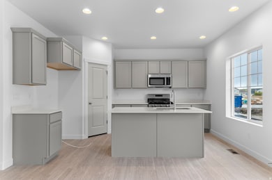 Kitchen featuring gray cabinetry, stainless steel appliances, recessed lighting, a center island with sink, and light wood-style flooring
