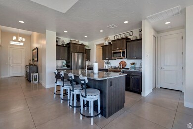 Kitchen with dark brown cabinetry, a kitchen bar, light tile patterned flooring, light stone counters, and stainless steel appliances